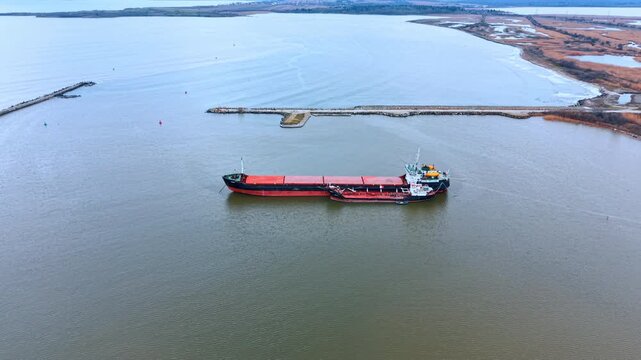 Two vessels in open water near the coastline. Cargo ship and a bunkering vessel side by side on the water with a dam and natural landscape background.