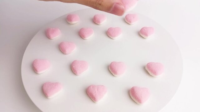 Hand arranging pink heart shaped gummy candies on white background for Valentines Day concept.
