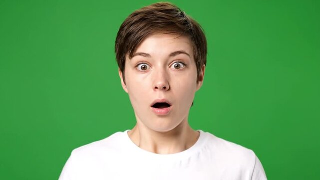 Surprised young woman with short brown hair looking up with an open mouth on a green background.