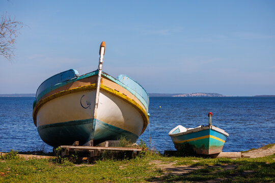 deux bateaux de p&ecirc;che abandonn&eacute;s sur un rivage, avec des traces de peinture &eacute;caill&eacute;e et des inscriptions, plac&eacute;s sur des supports en bois &agrave; proximit&eacute; de l'&eacute;tang de Salses-Leucate, sous un ciel clair.