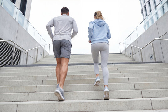 Fit couple in sportswear running up concrete city stairs during outdoor fitness workout
