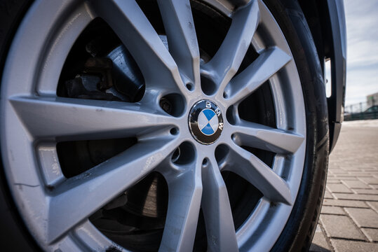 Close up focuses on the BMW roundel on a multi spoke alloy wheel, with brake caliper and rotor faintly visible, outdoors on pavement in soft daylight at a parking area.