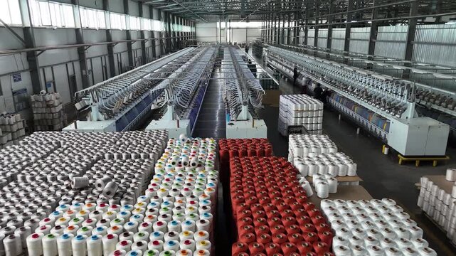 Large industrial textile factory interior with automated spinning machines and rows of yarn spools
