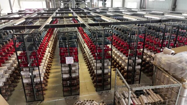 Large warehouse interior with rows of colorful yarn spools on racks in a textile factory