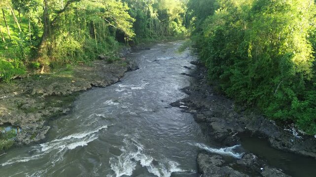 Scenic river landscape with a bridge, waterfall, and lush green forest at sunset