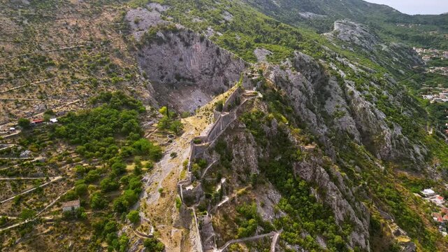 Aerial orbital view of the historic city walls and San Giovanni fortress winding up a steep mountain in Kotor, Montenegro
