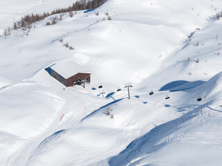Fototapeta premium Aerial view of San Domenico ski resort in the Italian Alps shows a wooden lift station, a chairlift crossing powder, faint ski and snowboard tracks, and sparse larch trees.