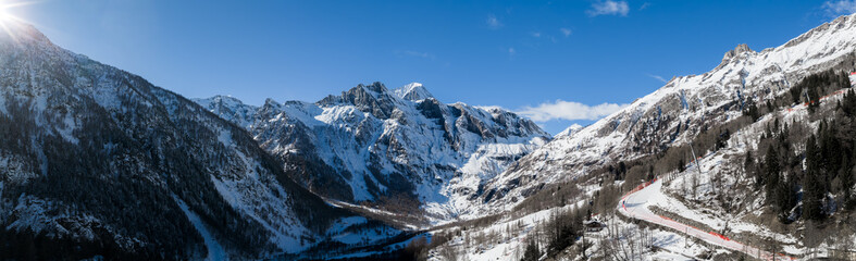 Fototapeta premium Aerial view shows San Domenico ski resort in the Italian Alps, with snow peaks, glacial valley, ski runs, chairlifts, winding road, resort buildings, and skiers.