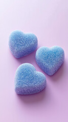 Fototapeta premium Three heart-shaped blue gummy candies sprinkled with sugar crystals are arranged on a soft pink surface, creating a sweet and delicate visual treat for all.