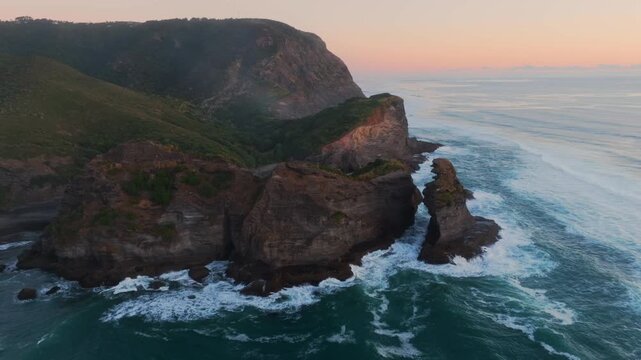 Aerial view of the rugged cliffs and sea stacks at Piha, Auckland, New Zealand, where the Tasman Sea meets the shore, creating a dramatic coastal landscape.