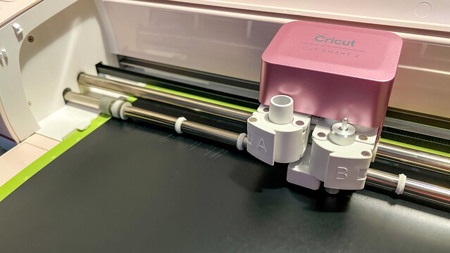 Cricut cutting machine with dual tool holder and black material on cutting mat, showcasing precision crafting technology for DIY projects