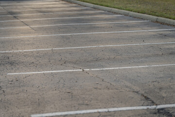 Fototapeta premium Empty parking spaces with white painted bay lines across cracked asphalt, bordered by a curb and grass strip in a quiet outdoor daylight scene