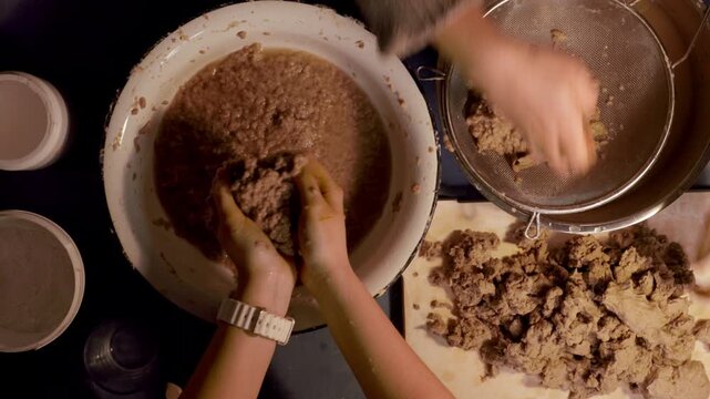 Step 2 of papier mache making process. Hands soaking torn egg carton pieces in water to soften recycled paper for craft pulp mixture. DIY recycled paper craft preparation