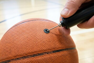 Fototapeta premium Hand inserting a metal needle from an air pump into a brown basketball