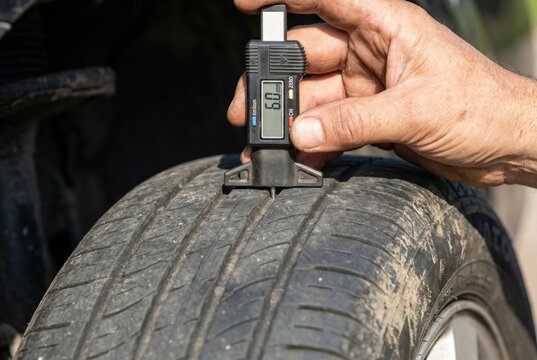 Mechanic hand using a digital depth gauge caliper to measure car tire tread wear