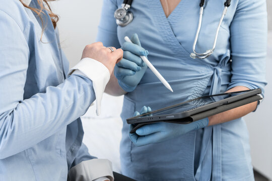 Doctors in medical attire discuss patient information while interacting with a touchscreen tablet and stylus. Digital tools streamline healthcare communication and improve efficiency