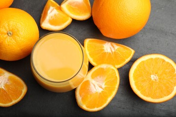 Fototapeta premium Citrus juice in glass and fresh oranges on black table, flat lay