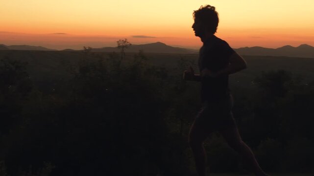 Silhouette of man running on grassy hill at golden hour sunset sunrise