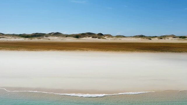 Vast ocean meets sandy beach, backed by brown grass and rolling dunes