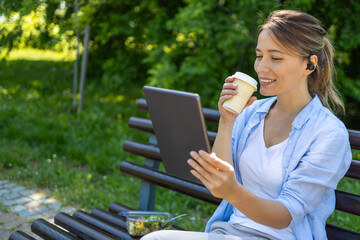Woman enjoying coffee and tablet on park bench, healthy lunch nearby © SISMIZ