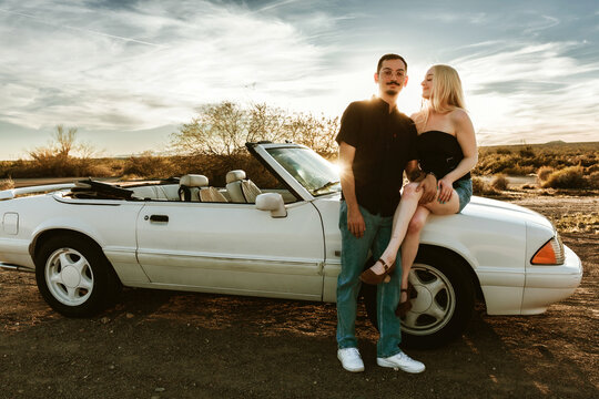 Couple standing and sitting on classic convertible