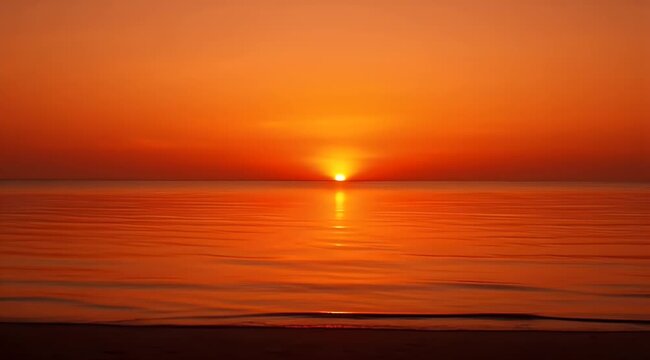 Golden sun dips into the ocean, casting fiery reflections on calm water and wet sand