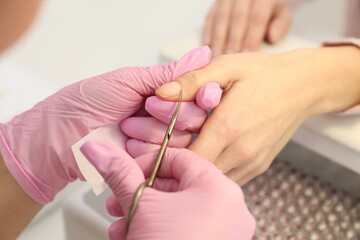 Professional manicurist cutting client's cuticle in beauty salon, closeup
