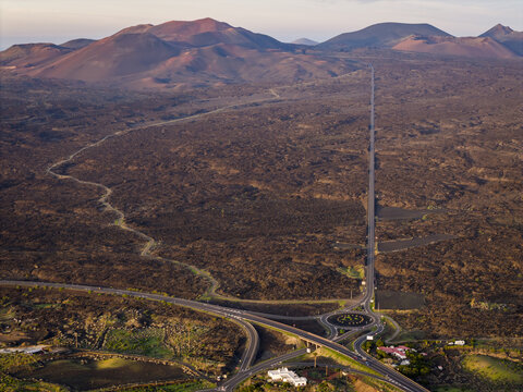 Aerial view of stark volcanic earth meets a meticulously planned road network near Timanfaya National Park, Lanzarote, Canarias, Spain.