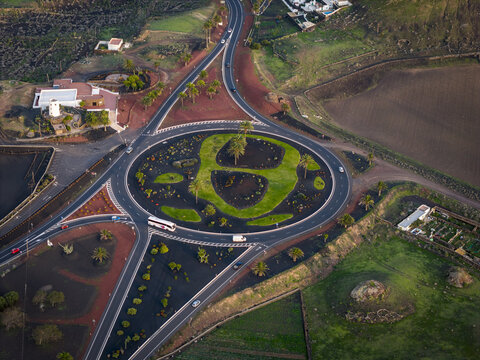 Aerial view of a roundabout with lush green grass and palm trees contrasting with the surrounding black volcanic rock, Lanzarote, Canarias, Spain.