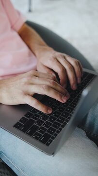 Close up hands types on laptop while sitting in a chair indoors during daytime with natural light coming through the window