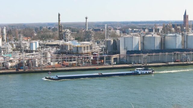 covered hold white wheelhouse stand out against refinery stacks rippling water reflects industrial skyline along canal zelzate maritime transport shipping channel surface 