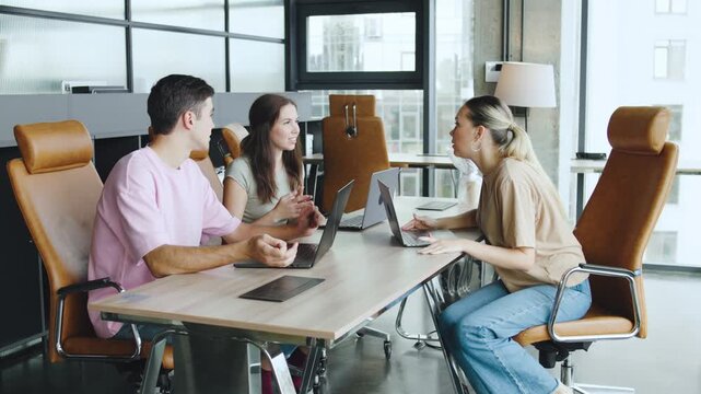 Meeting IT professionals takes place in a modern office with three people discussing work on laptops during daylight hours,customer support