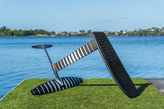 Black carbon fibre dock start pump foiling hydrofoil board and hydrofoil on dock covered in artificial grass with a calm blue lake in the background. Sunny clear blue sky.