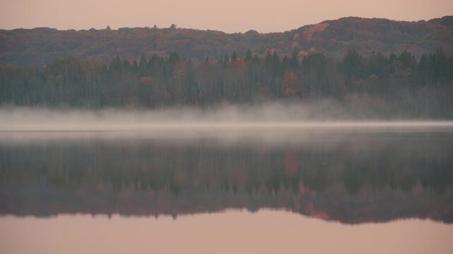 Panoramic sunrise view of autumn forest hills and calm lake, cinematic morning light on vibrant yellow and orange fall foliage with still water reflection