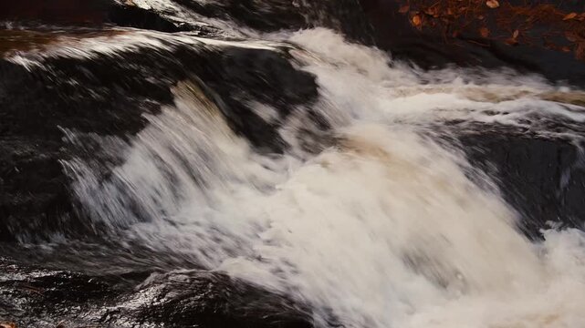 Powerful waterfall rushing over dark river rocks, close up of white water rapids with motion blur, scenic natural stream in autumn forest