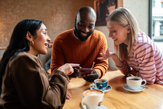 Three friends laughing over smartphone at cafe