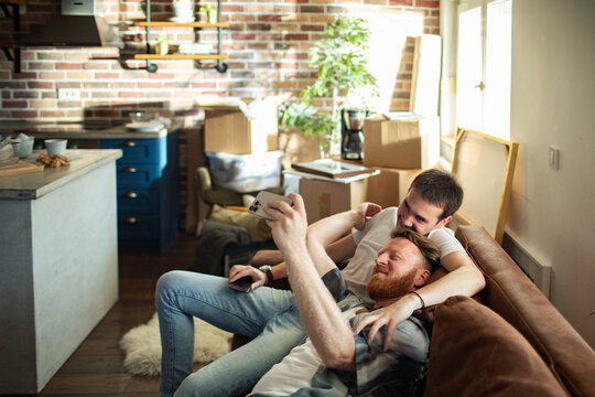 Two men taking selfie on sofa in new apartment