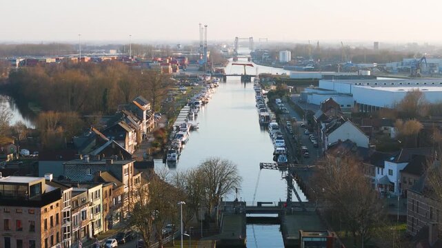 pleasure boats densely line klein willebroek canal beneath brick stucco houses converging container yards steel drawbridges under pale misty morning sky toward dense lining 