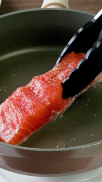 Cooking pan seared salmon moment, sliced salmon with rosemary in nonstick teflon coating pan with garlic, vegetables.