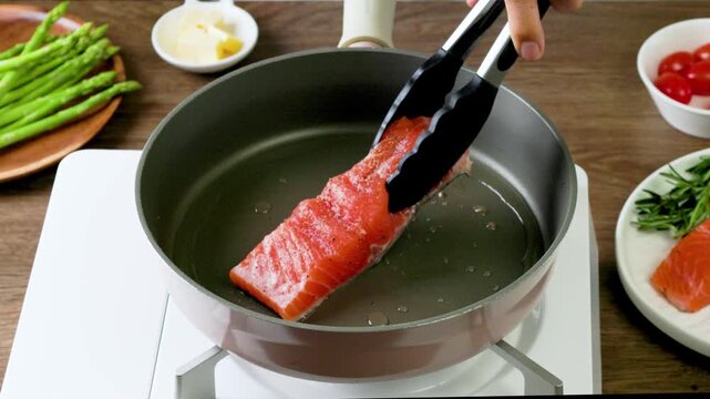 Cooking pan seared salmon moment, sliced salmon with rosemary in nonstick teflon coating pan with garlic, vegetables.