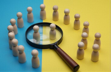 Fototapeta premium Wooden figures surround a magnifying glass symbolizing selection or
