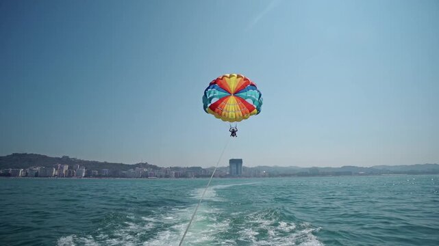 People parasailing over crystalline blue sea pulled by yacht boat with colorful parachute on a sunny day