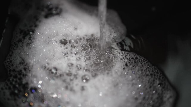 Close-up of soapy foam and water streaming in a kitchen sink setting
