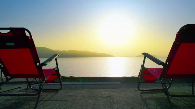 Two red sunbeds are positioned on a terrace overlooking a serene ocean view at sunset