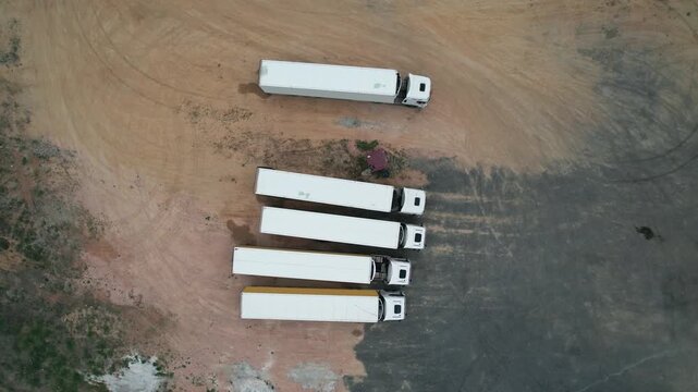 Aerial view of parked white trucks on a dry terrain parking area