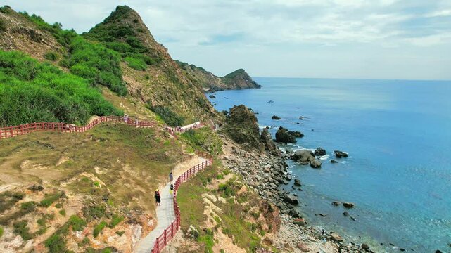 High-angle 4K drone tracking along the Eo Gio mountainside, showing seaside walking paths and rocky beaches with turquoise water.