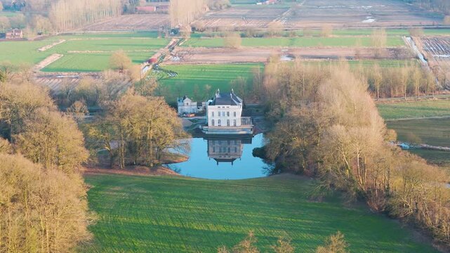 ch teau style mansion rests small island surrounded by reflective pond manicured lawns bare winter trees patchwork farmland extend into soft golden countryside horizon teau-style 