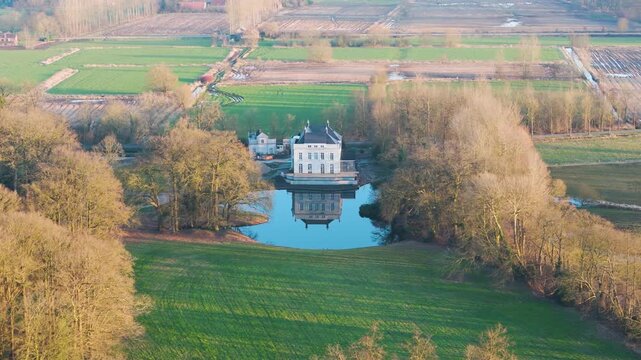 manor slate roof symmetrical facade rises above moat like pond bare branched trees rolling emerald fields fade into cultivated farmland beyond countryside scene fa ade 