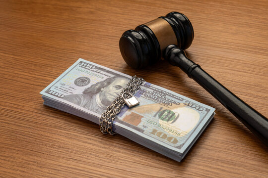 A judge's gavel next to a stack of money bound by a metal chain and secured with a padlock. Legal financial restrictions, asset seizure, bail money, court-ordered settlements concept.