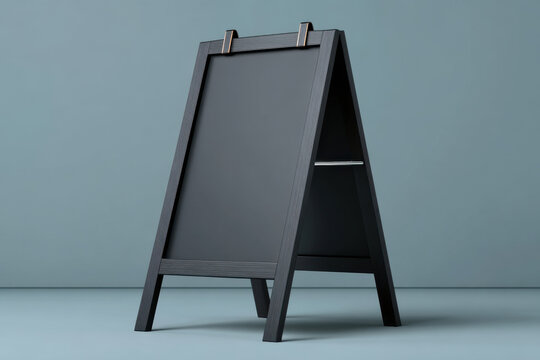 Blank sidewalk chalkboard sign on frame stand in studio setting with muted blue background and soft lighting, minimalist promotional display for menu or advertising